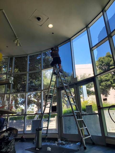 Installer on a ladder applying window film to tall commercial windows